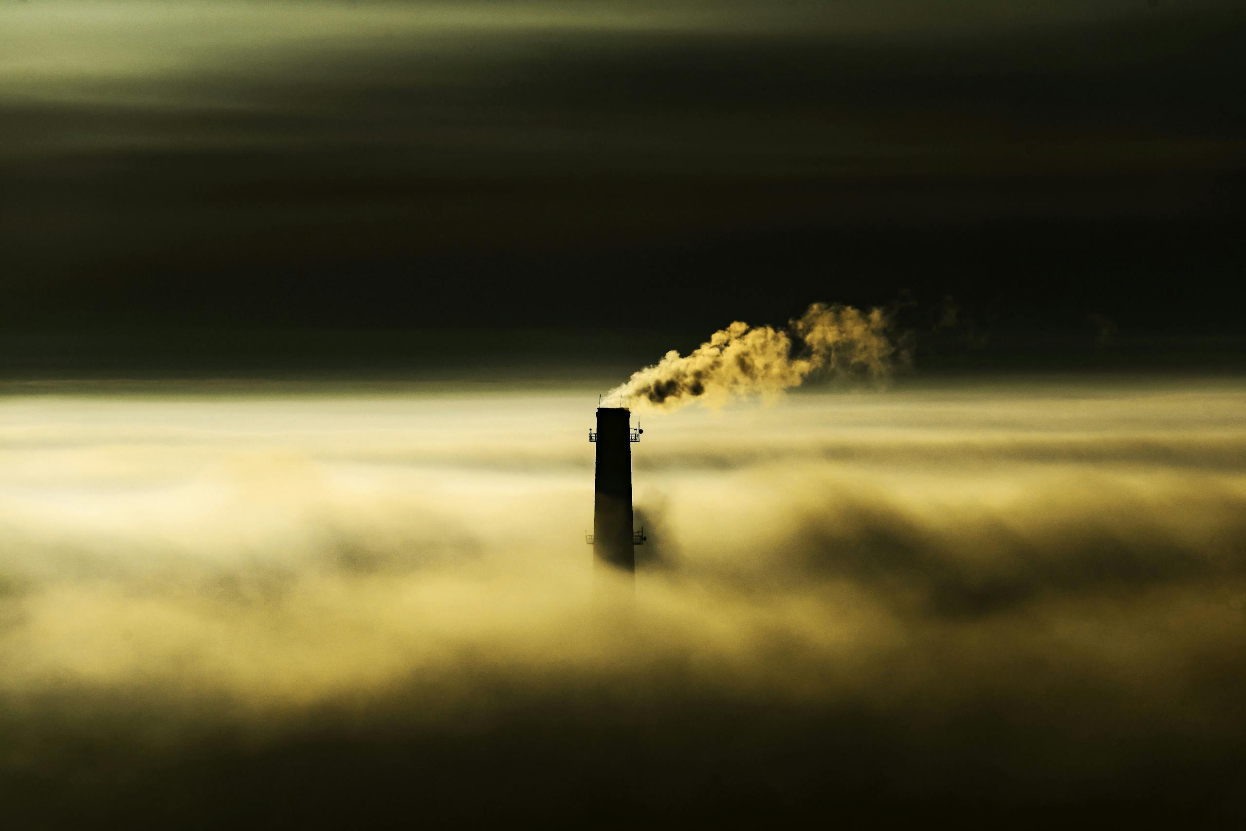 An Industrial Chimney Over a Thick Fog Emitting Smoke