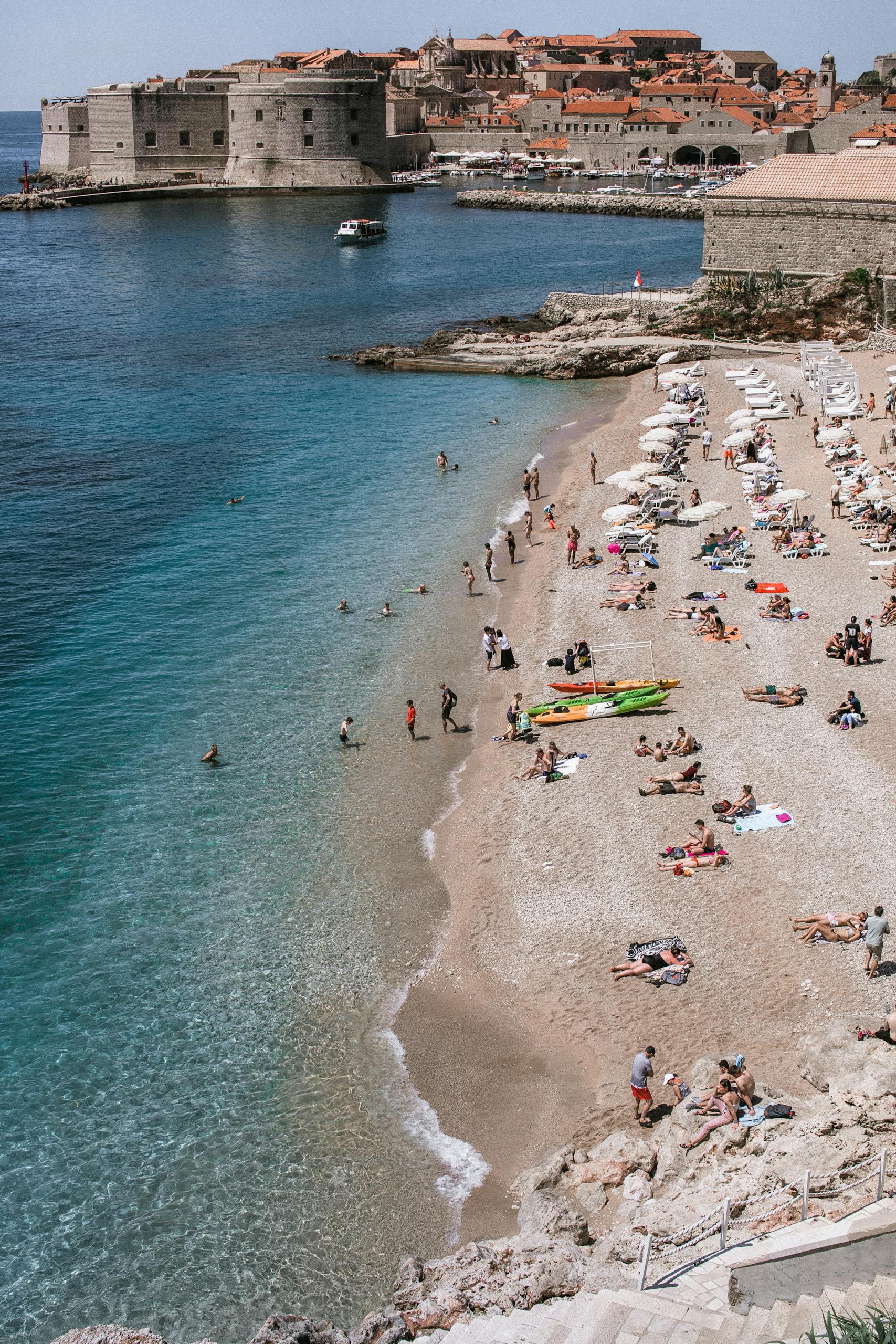 High angle of faceless tourists resting on sandy sea coast against ancient buildings in Dubrovnik Croatia