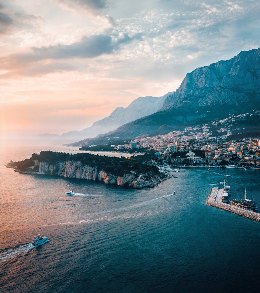 Scenic aerial shot of Makarska, Croatia capturing the coastline, island, and majestic mountains at sunset.