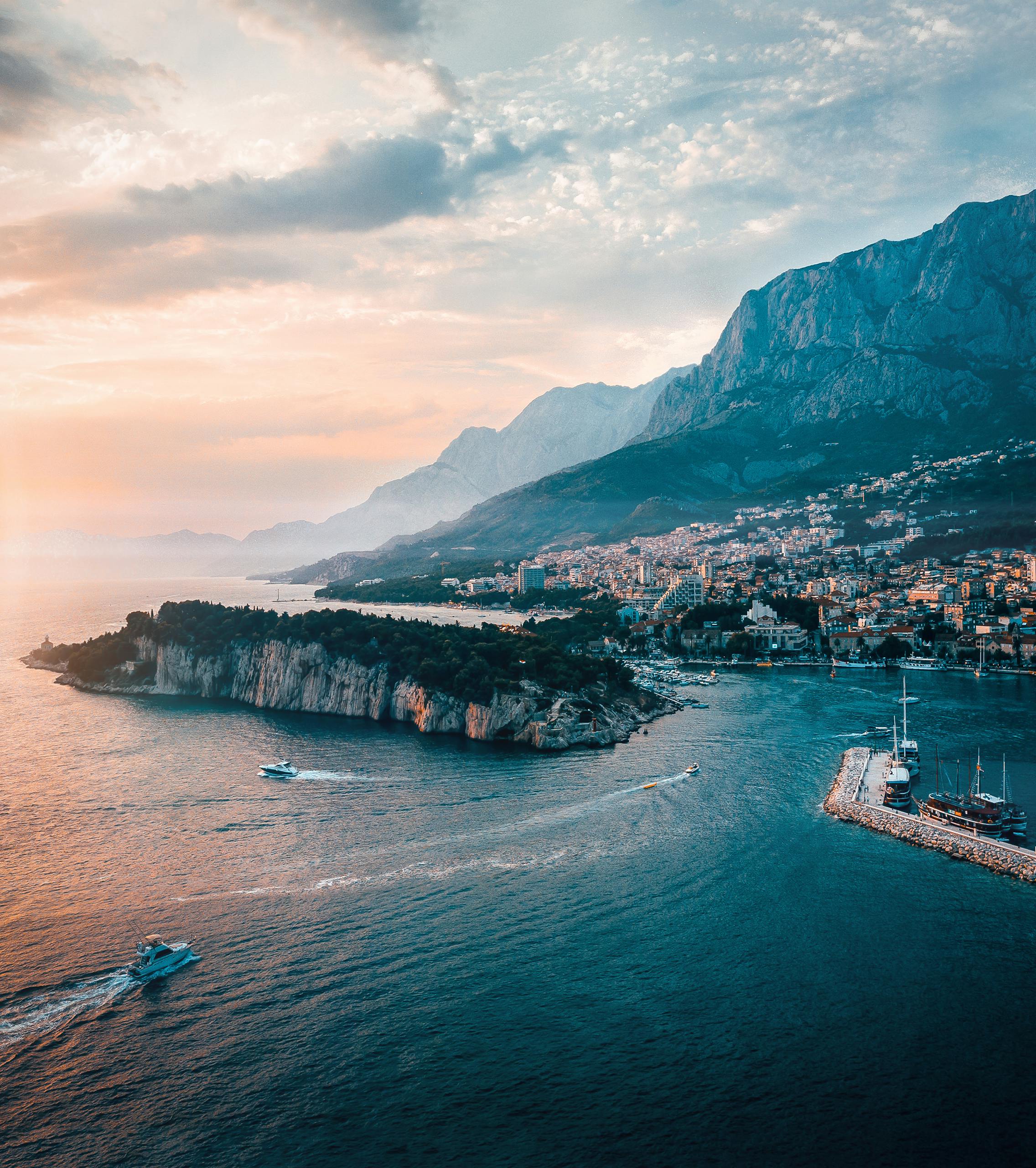 Scenic aerial shot of Makarska, Croatia capturing the coastline, island, and majestic mountains at sunset.