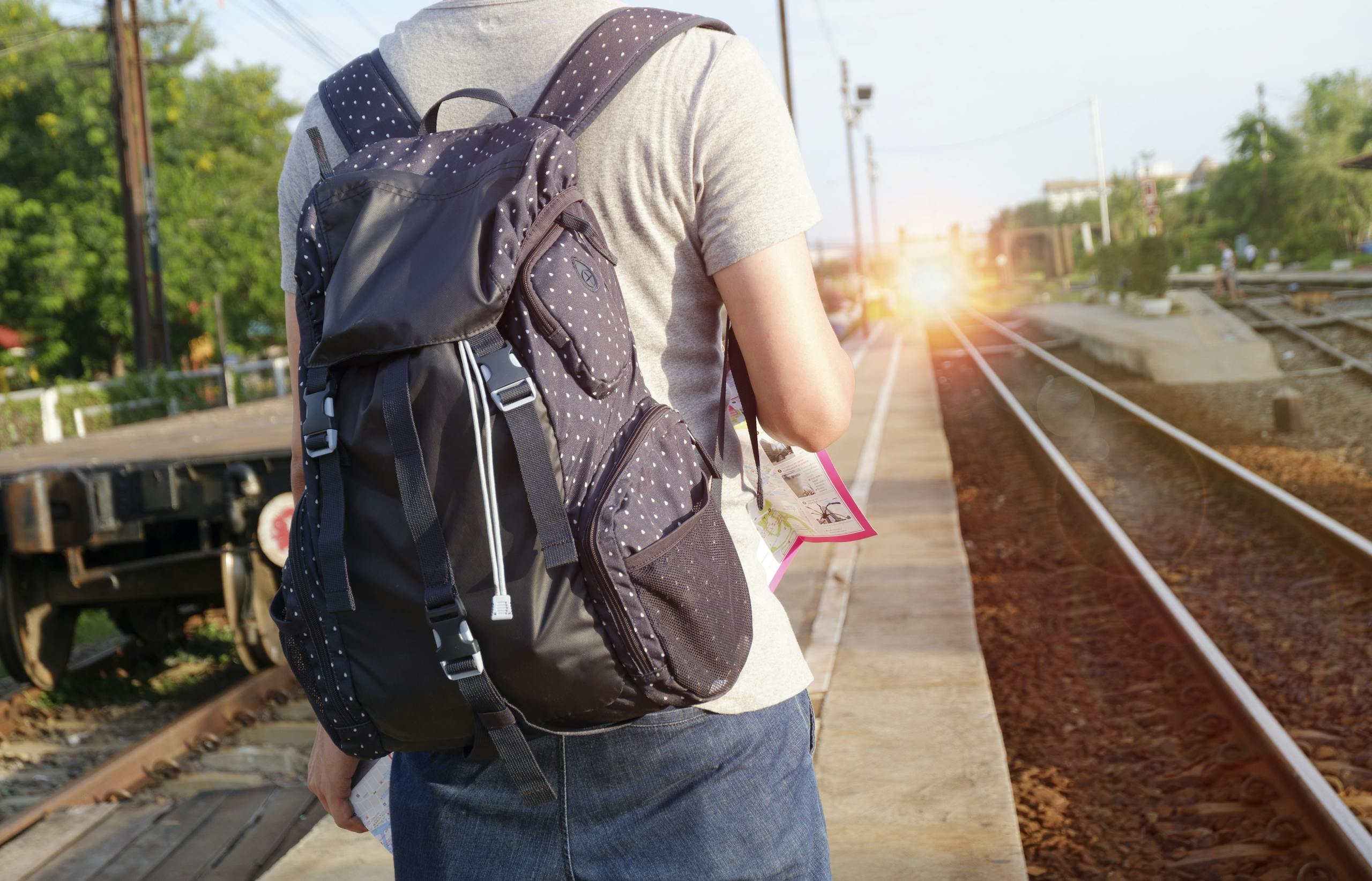 A person with a backpack waits at a railway station during daytime.