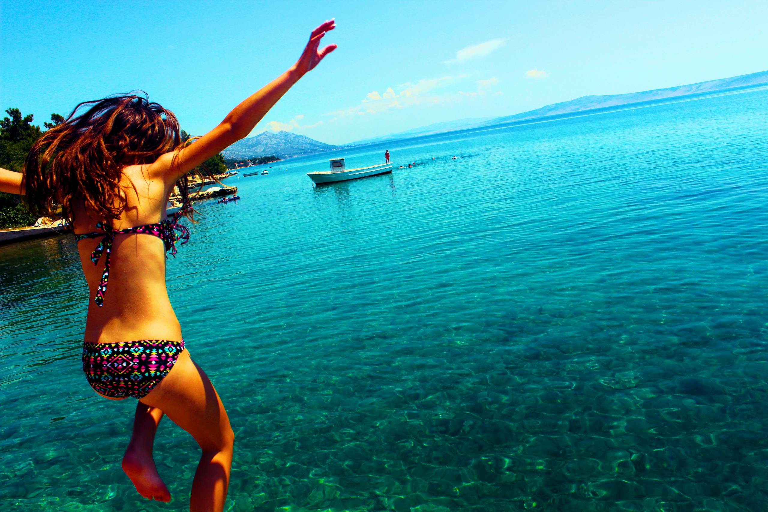 Young woman in a bikini jumps into crystal clear Croatian sea, enjoying summer vacation.