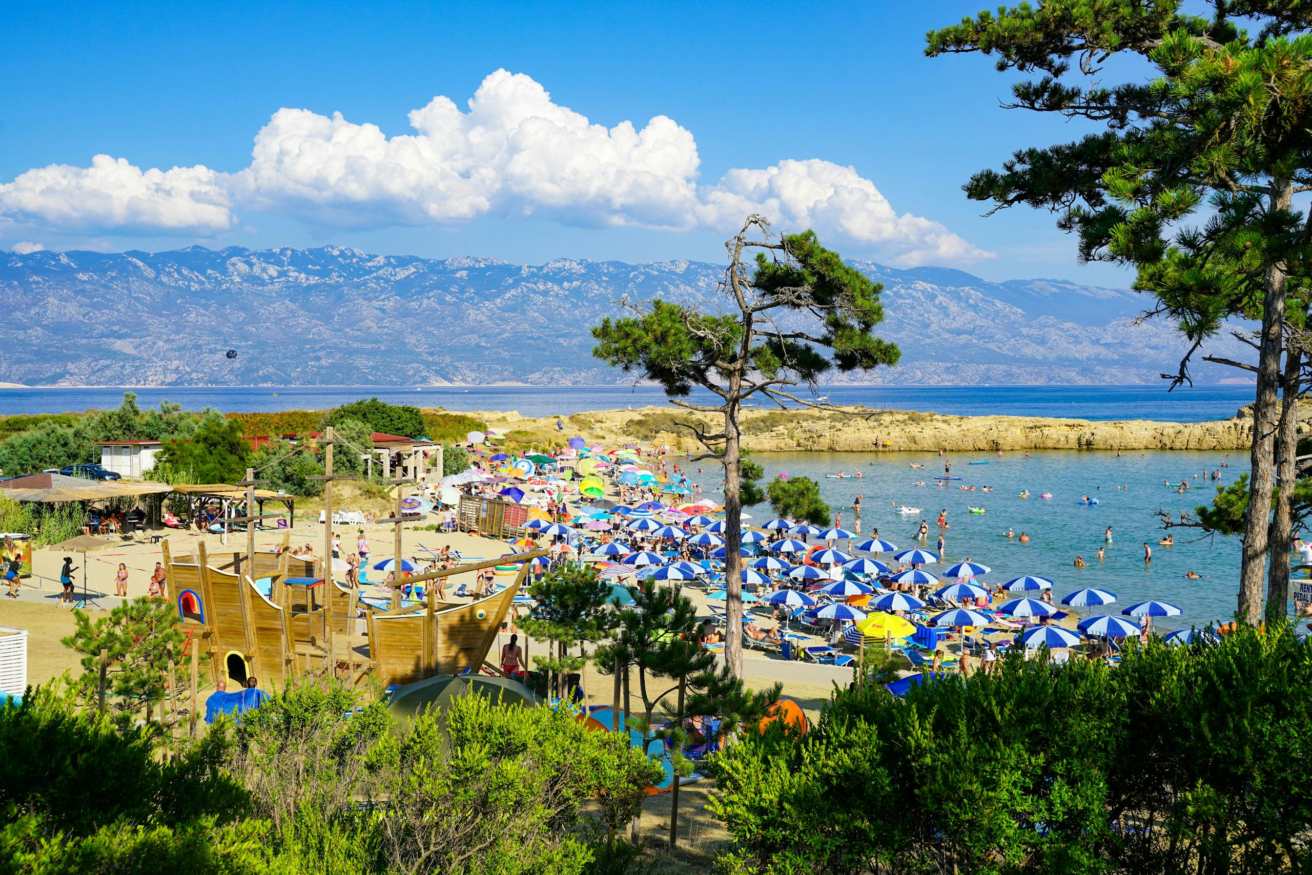 Enjoy a sunny day on the bustling beach of Lopar, Croatia, with mountains in view.