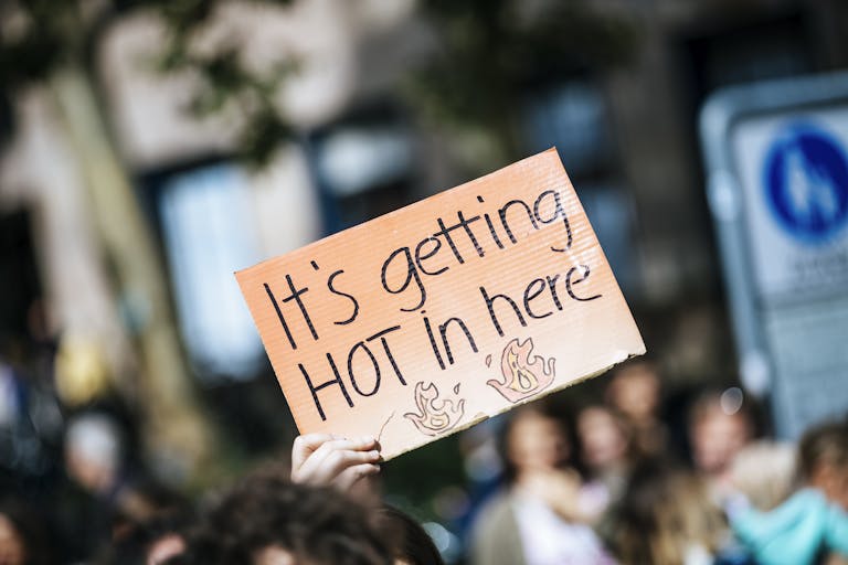 Hand holding a "It's getting hot in here" sign at a climate protest, emphasizing global warming.